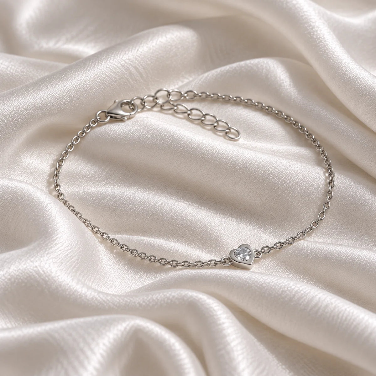 Heart_bracelet_in_sterling_silver_with_a_small_CZ_stone_at_side_angle_view_on_soft_fabric_background