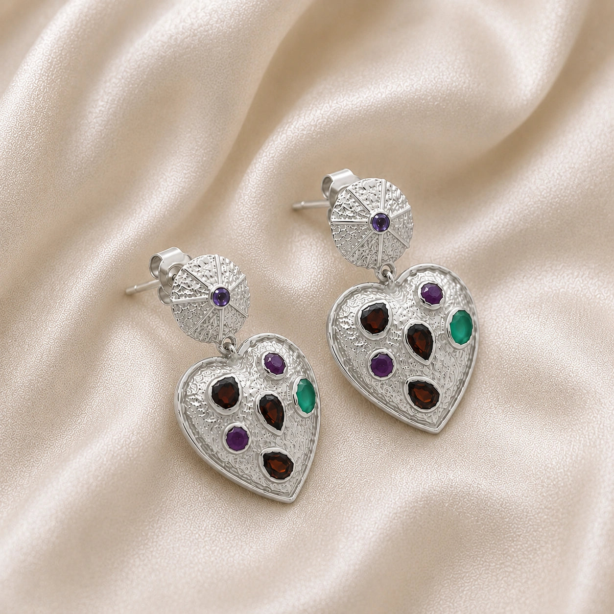 Heart_earrings_in_sterling_silver_with_garnet_ruby_and_green_onyx_stones_slightly_angled_on_soft_fabric_background