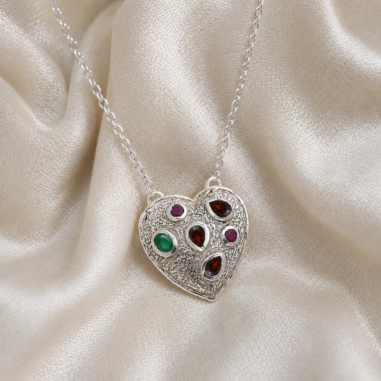 Heart_locket_necklace_sterling_silver_with_garnet_ruby_and_green_onyx_stones_in_front_angle_view_on_soft_fabric_background