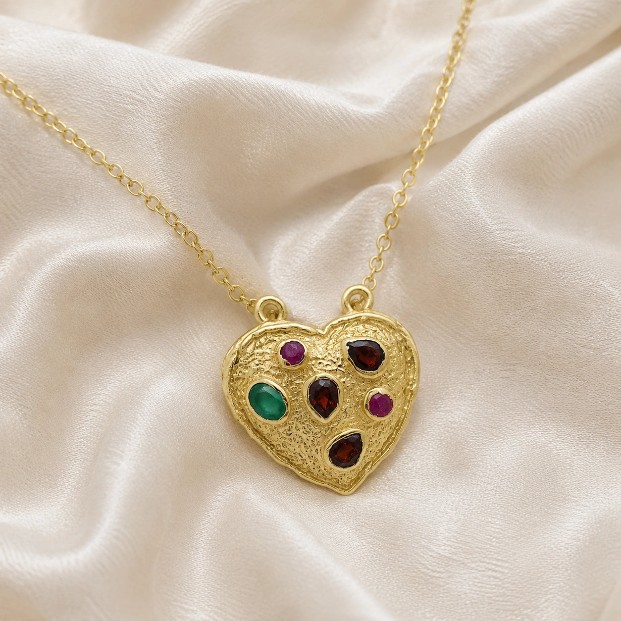 Heart_locket_necklace_gold_plated_silver_with_garnet_ruby_and_green_onyx_stones_in_front_angle_view_on_soft_fabric_background