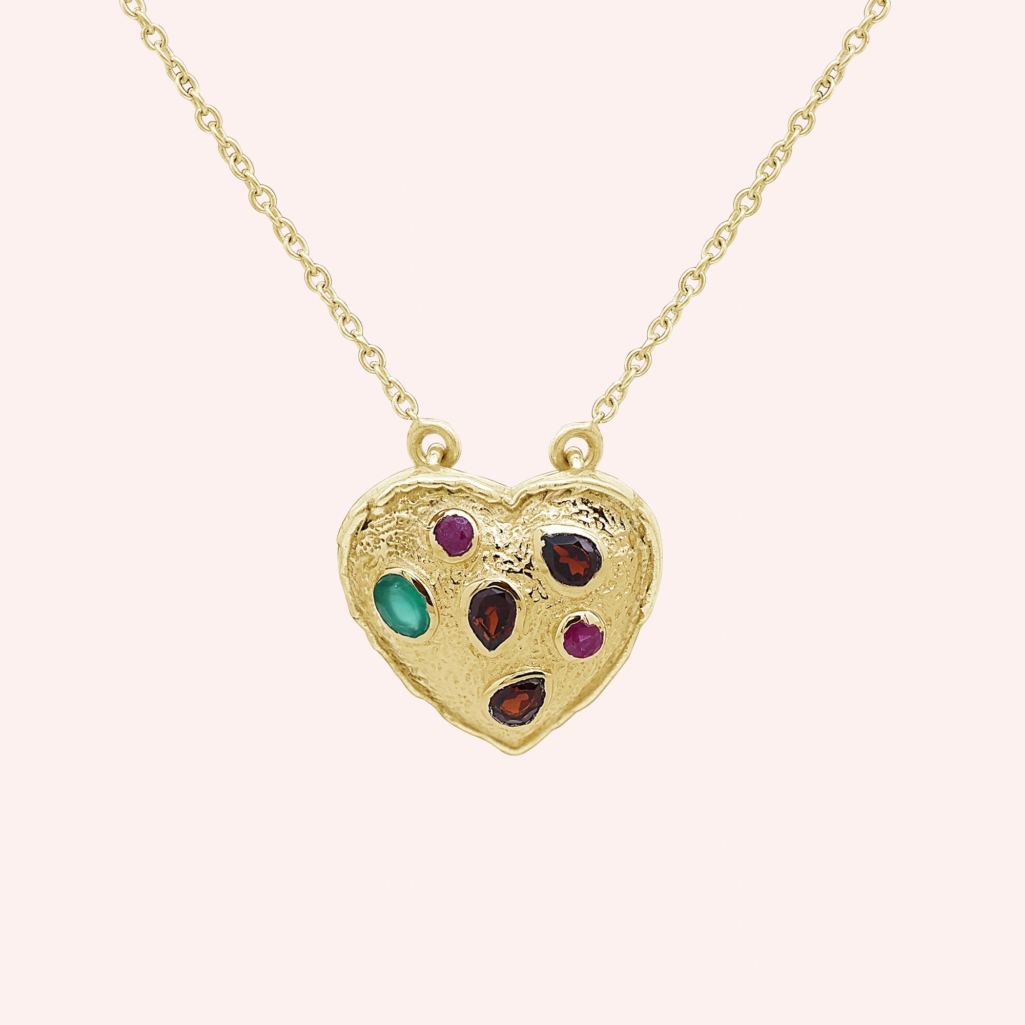 Heart_locket_necklace_gold_plated_silver_with_garnet_ruby_and_green_onyx_stones_in_front_angle_view_on_solid_pink_background