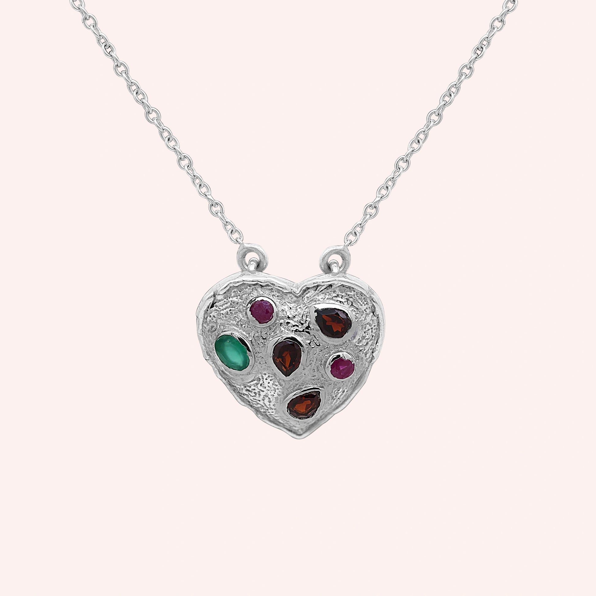 Heart_locket_necklace_sterling_silver_with_garnet_ruby_and_green_onyx_stones_in_front_angle_view_on_solid_pink_background