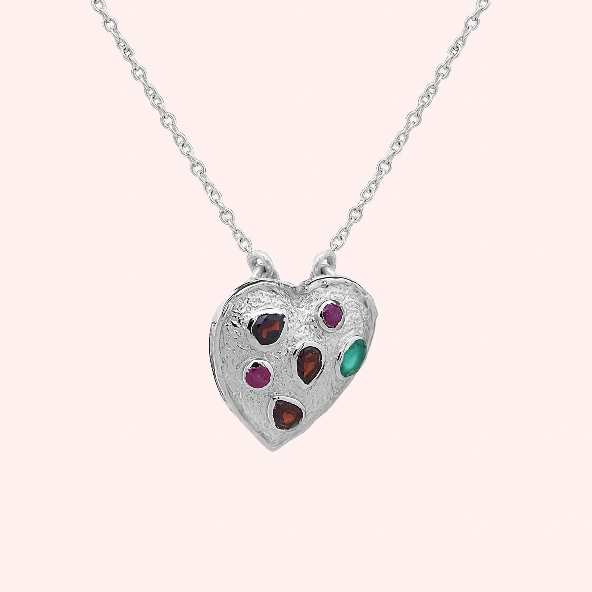 Heart_locket_necklace_sterling_silver_with_garnet_ruby_and_green_onyx_stones_in_slight_angle_view_on_solid_pink_background