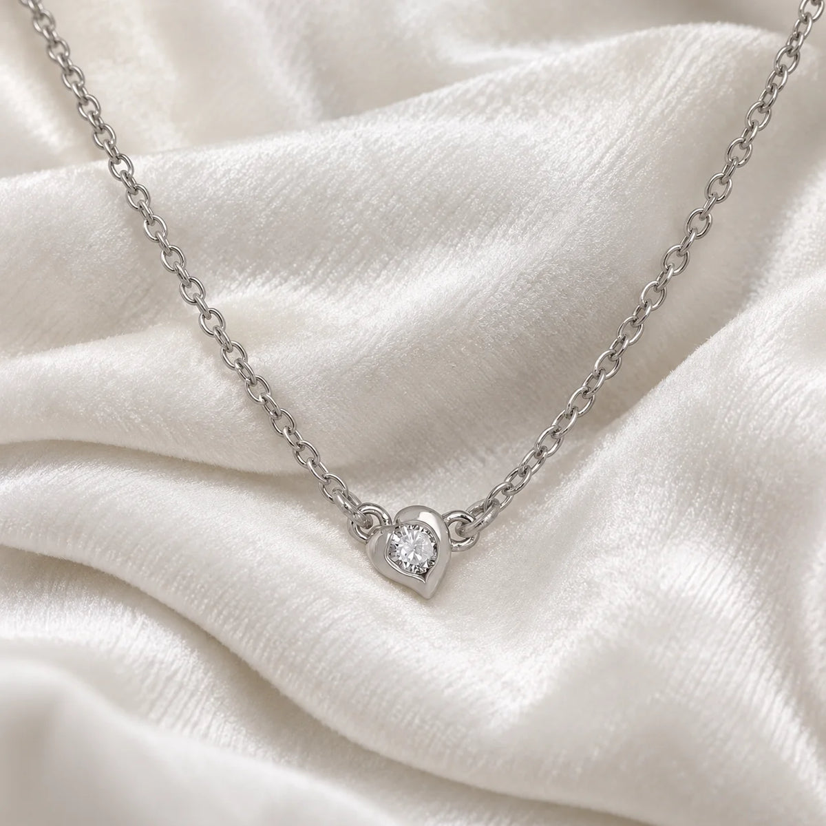Heart_necklace_in_sterling_silver_with_a_small_round_CZ_stone_at_front_angle_view_on_soft_fabric_background