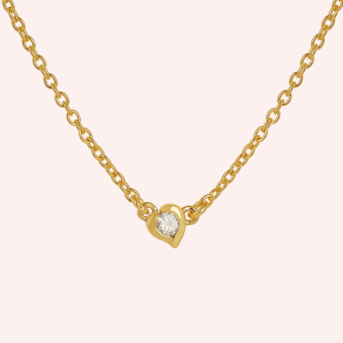 Heart_necklace_in_gold_plated_silver_with_a_small_round_CZ_stone_at_front_angle_view_on_solid_pink_background