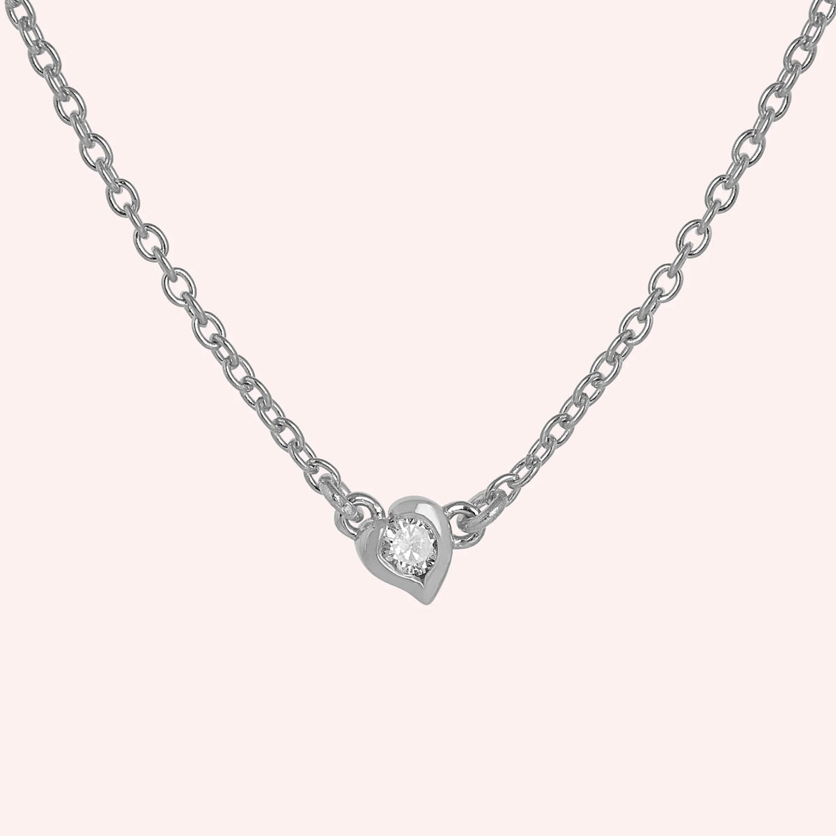 Heart_necklace_in_sterling_silver_with_a_small_round_CZ_stone_at_front_angle_view_on_solid_pink_background