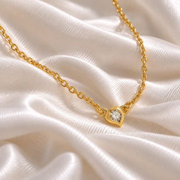 Heart_necklace_in_gold_plated_silver_with_a_small_round_lab_grown_diamond_at_side_angle_view_on_soft_fabric_background