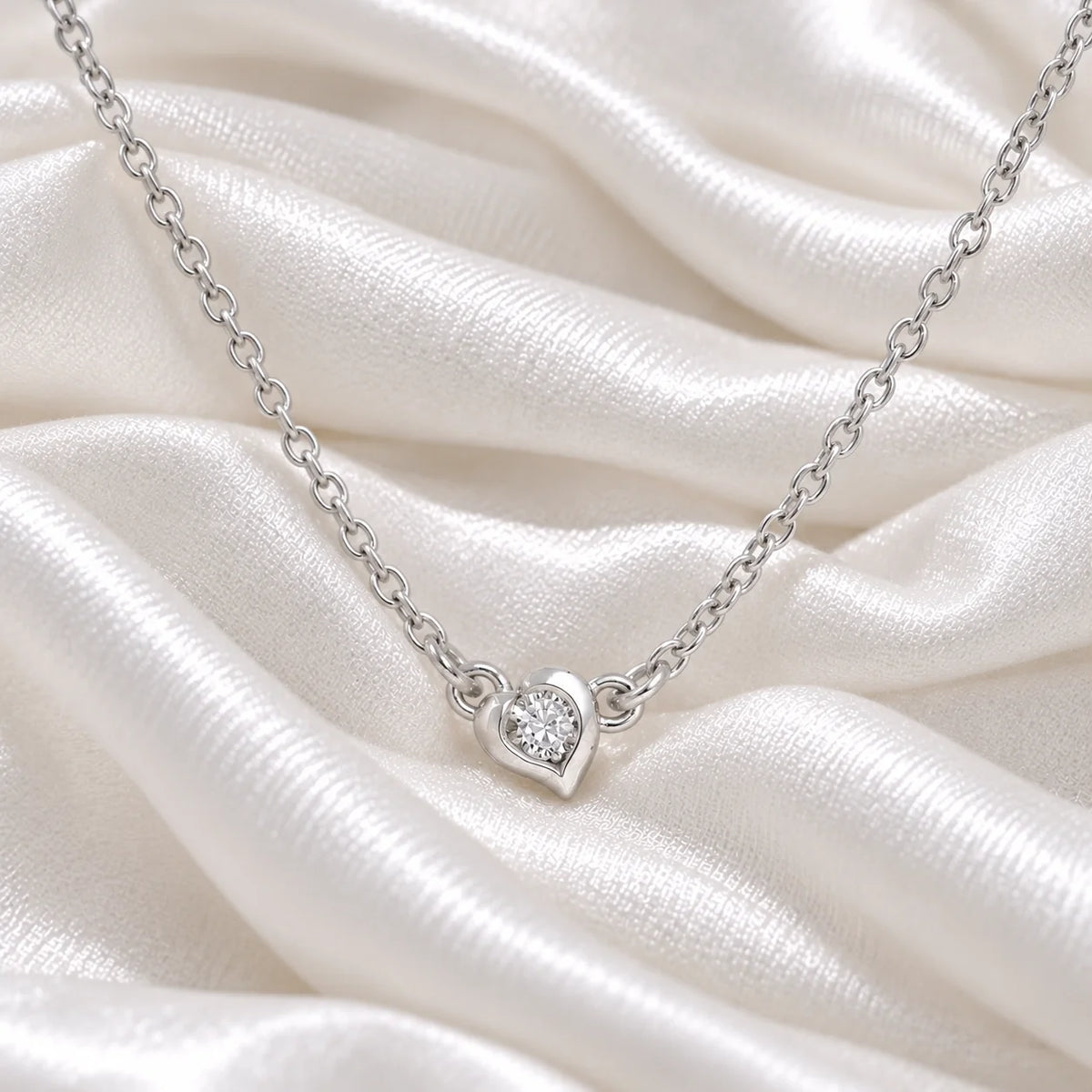 Heart_necklace_in_sterling_silver_with_a_small_round_lab_grown_diamond_at_front_angle_view_on_soft_fabric_background