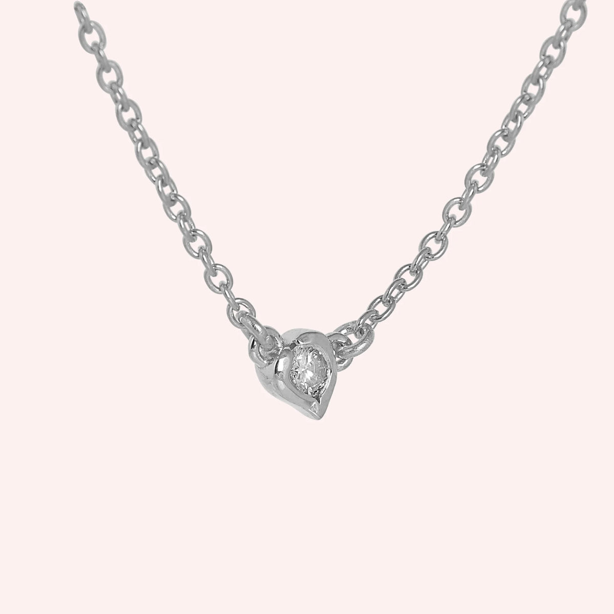 Heart_necklace_in_sterling_silver_with_a_small_round_CZ_stone_at_side_angle_view_on_solid_pink_background