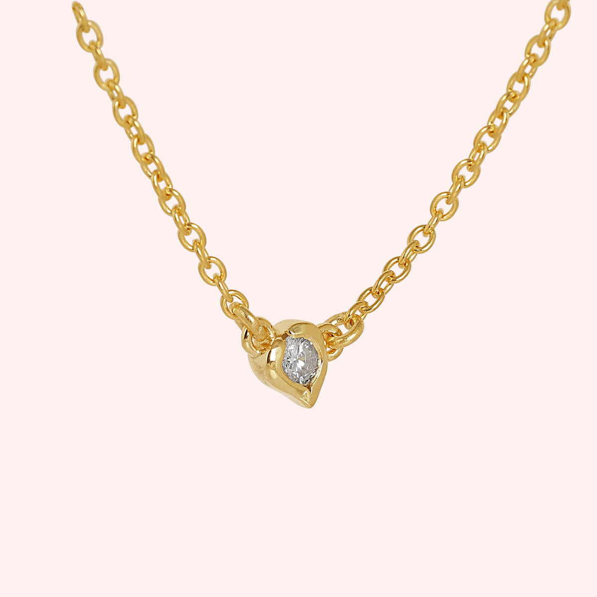Heart_necklace_in_gold_plated_silver_with_a_small_round_CZ_stone_at_side_angle_view_on_solid_pink_background