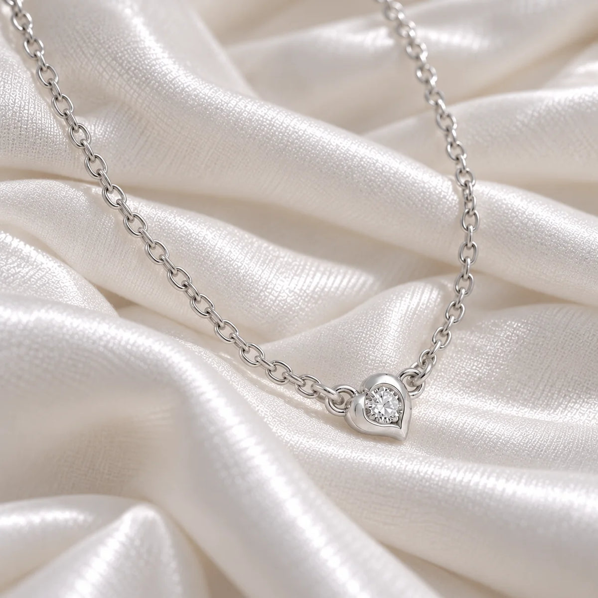 Heart_necklace_in_sterling_silver_with_a_small_round_lab_grown_diamond_at_side_angle_view_on_soft_fabric_background