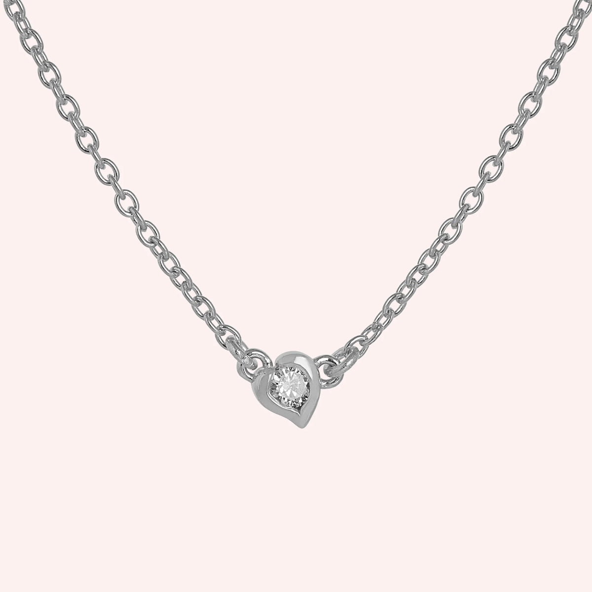 Heart_necklace_in_sterling_silver_with_a_small_round_lab_grown_diamond_at_front_angle_view_on_solid_pink_background