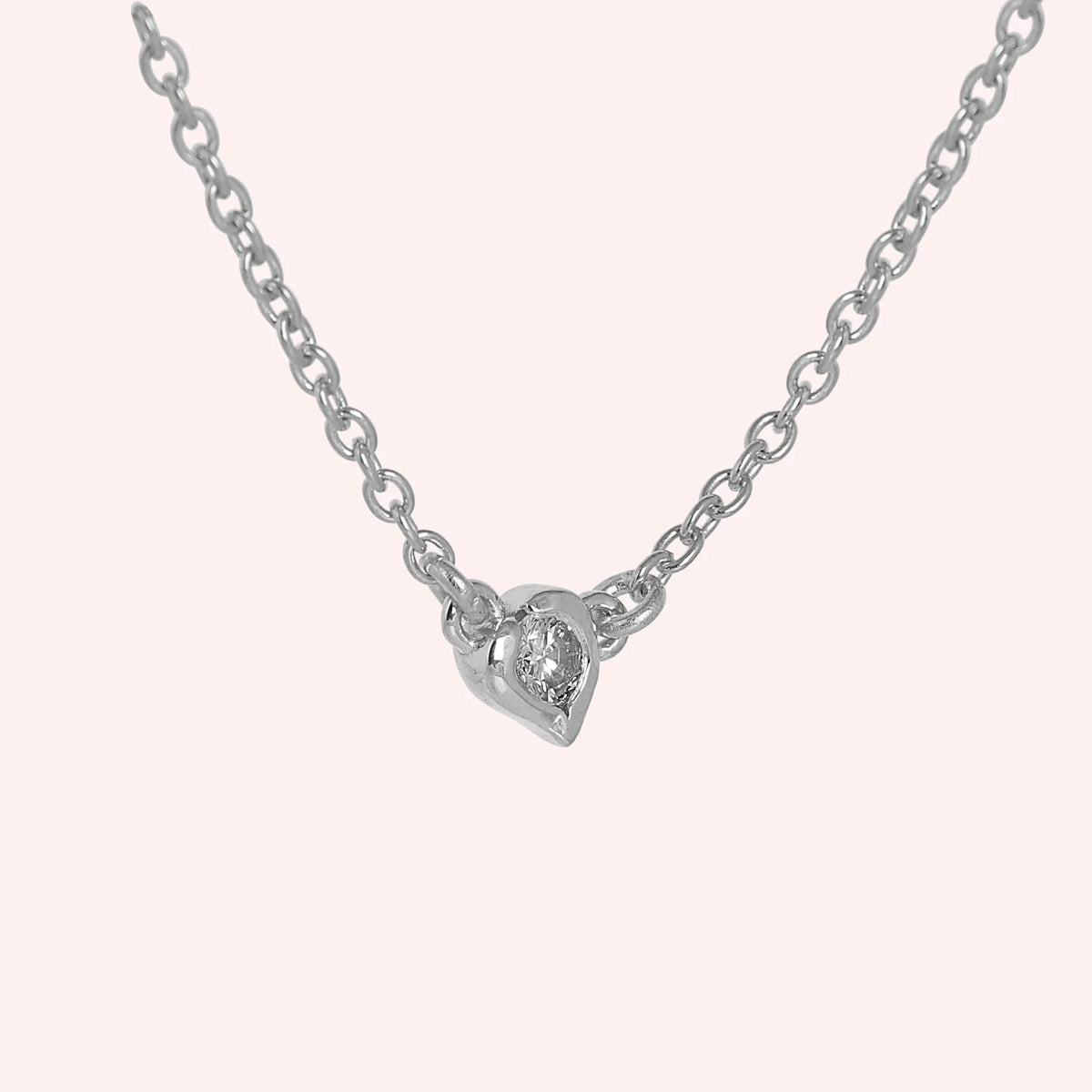 Heart_necklace_in_sterling_silver_with_a_small_round_lab_grown_diamond_at_side_angle_view_on_solid_pink_background