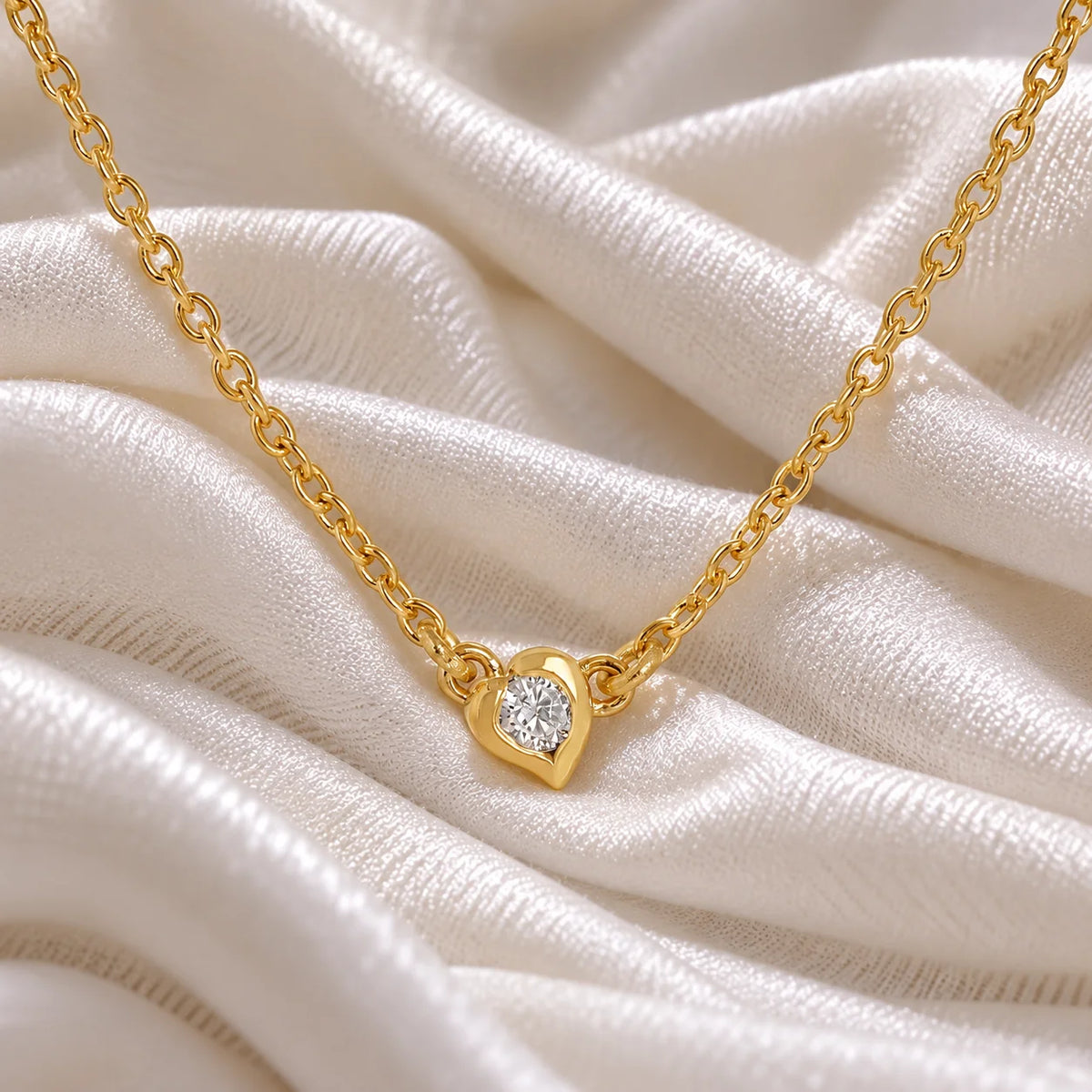 Heart_necklace_in_gold_plated_silver_with_a_small_round_CZ_stone_at_front_angle_view_on_soft_fabric_background