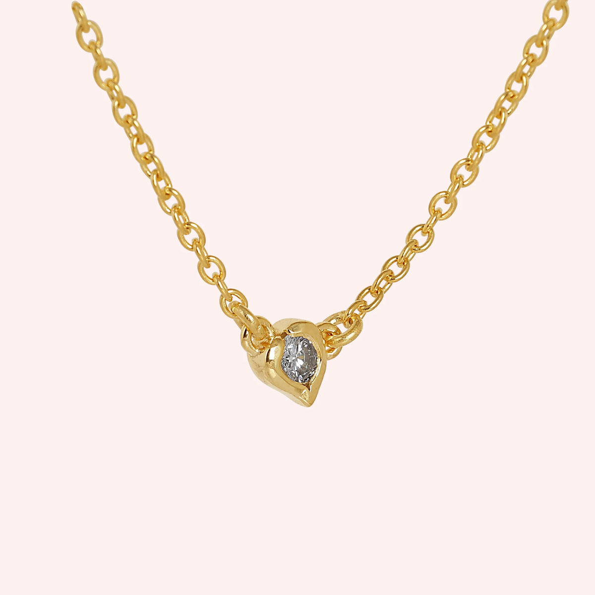 Heart_necklace_in_gold_plated_silver_with_a_small_round_lab_grown_diamond_at_side_angle_view_on_solid_pink_background