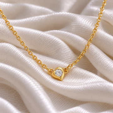 Heart_necklace_in_gold_plated_silver_with_a_small_round_CZ_stone_at_side_angle_view_on_soft_fabric_background