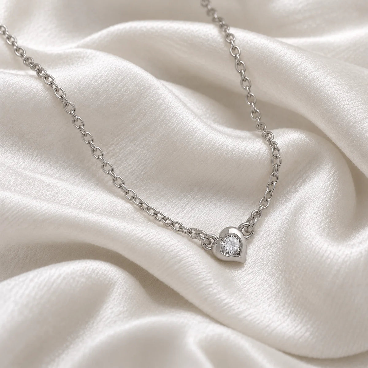 Heart_necklace_in_sterling_silver_with_a_small_round_CZ_stone_at_side_angle_view_on_soft_fabric_background