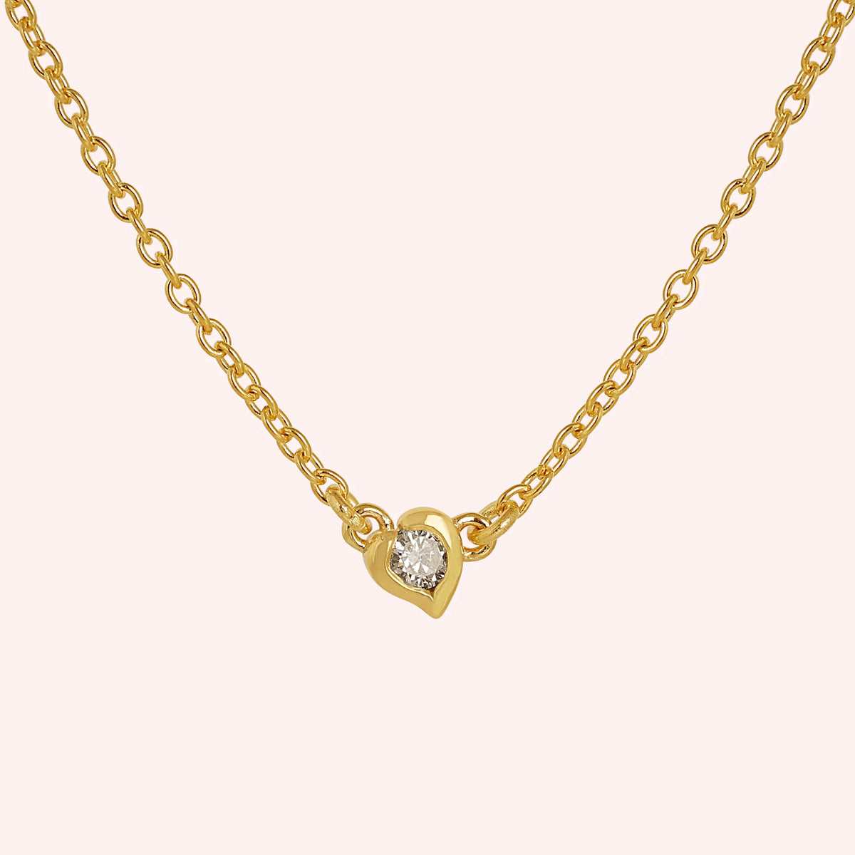 Heart_necklace_in_gold_plated_silver_with_a_small_round_lab_grown_diamond_at_front_angle_view_on_solid_pink_background