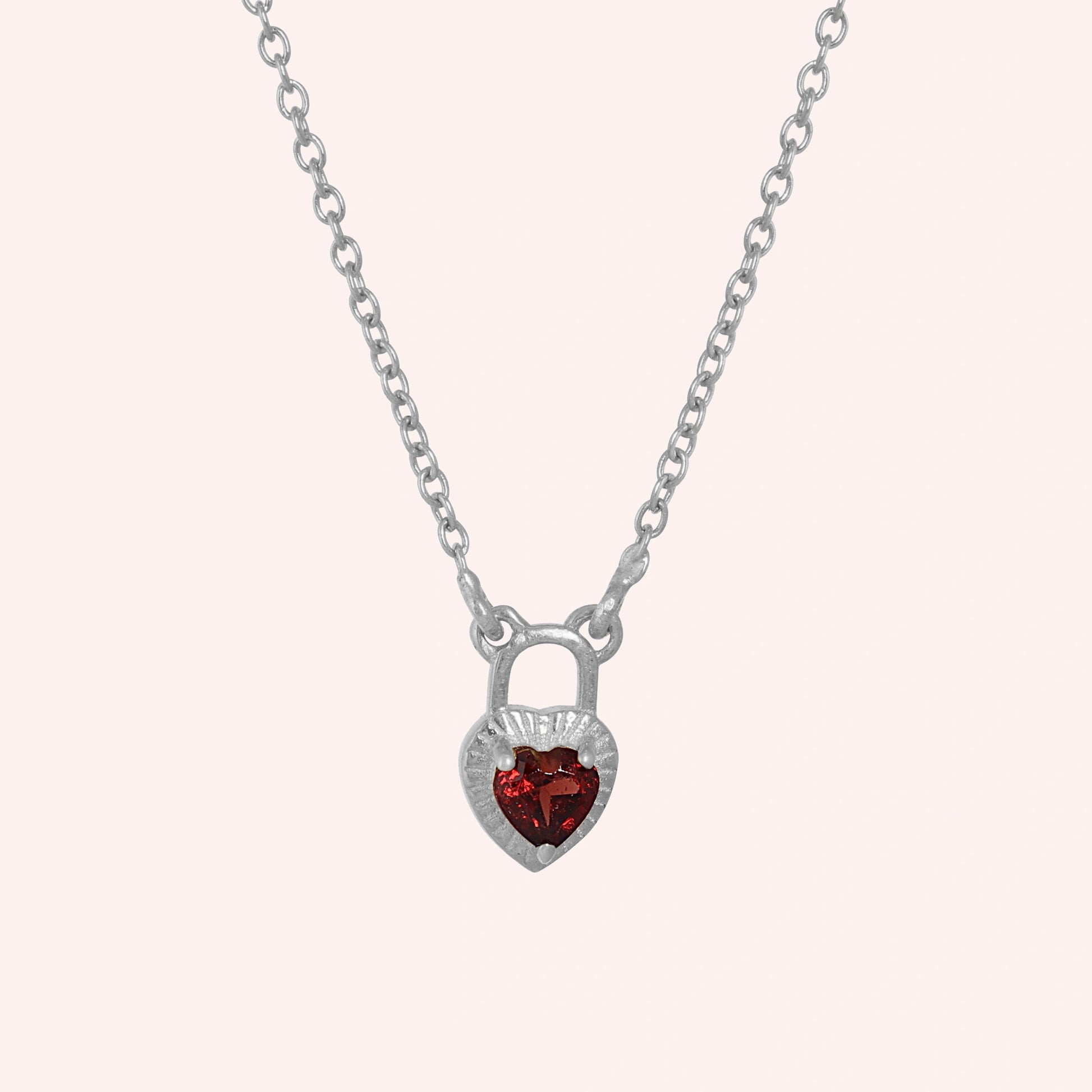 Heart_pendant_necklace_in_sterling_silver_front_angle_with_lock_design_and_garnet_stone_charm_on_solid_pink_background