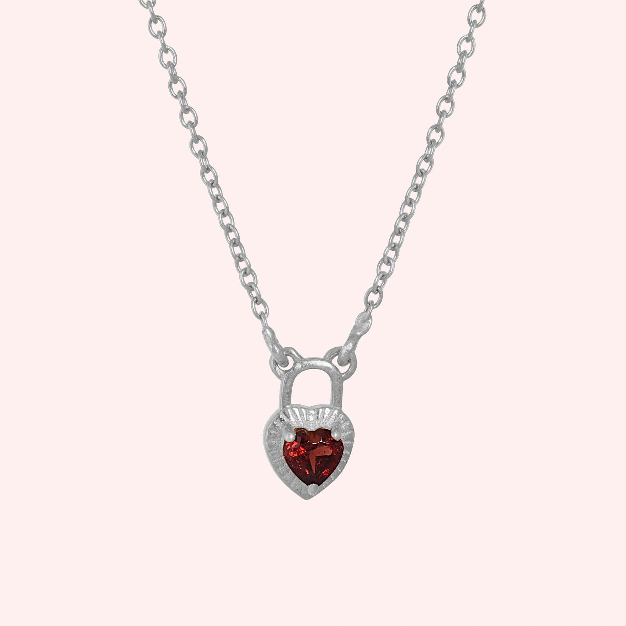 Heart_pendant_necklace_in_sterling_silver_front_angle_with_lock_design_and_garnet_stone_charm_on_solid_pink_background