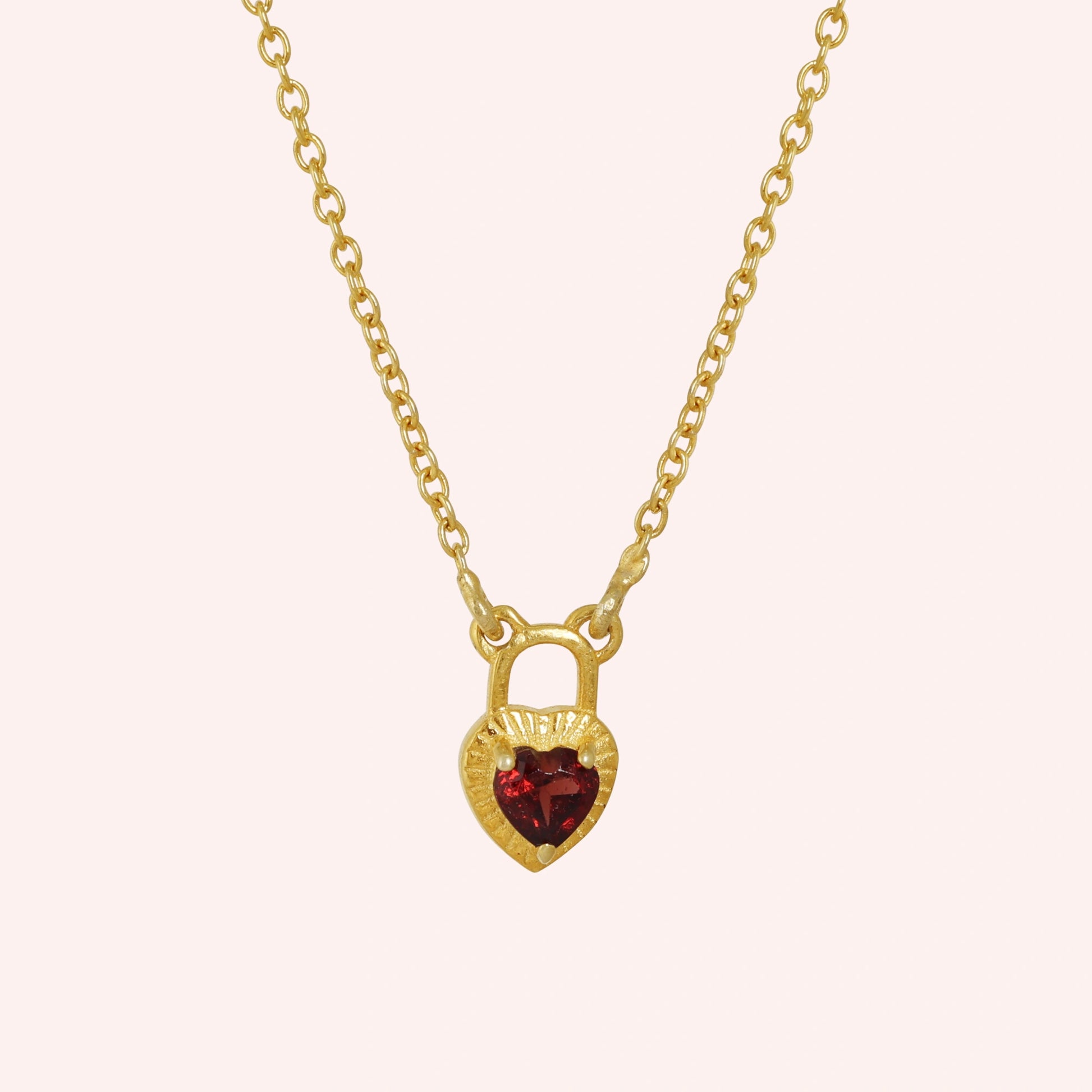 Heart_pendant_necklace_in_gold_plated_silver_front_angle_with_lock_design_and_garnet_stone_charm_on_solid_pink_background