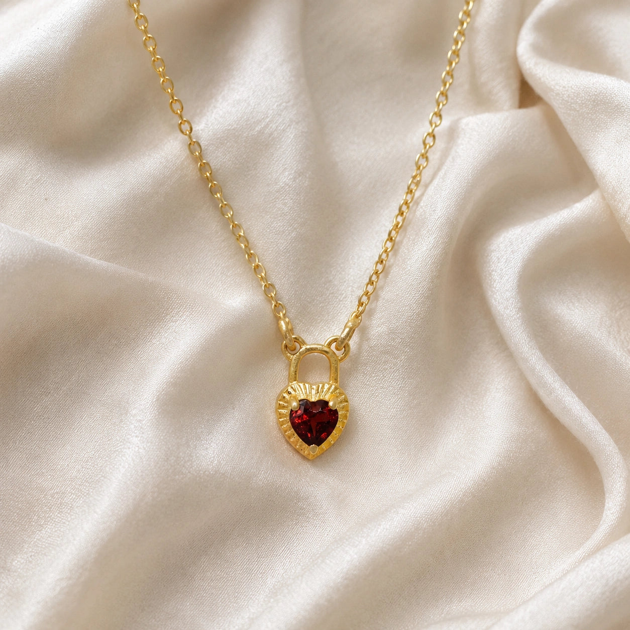 Heart_pendant_necklace_in_gold_plated_silver_front_angle_with_lock_design_and_garnet_stone_charm_on_soft_fabric_background