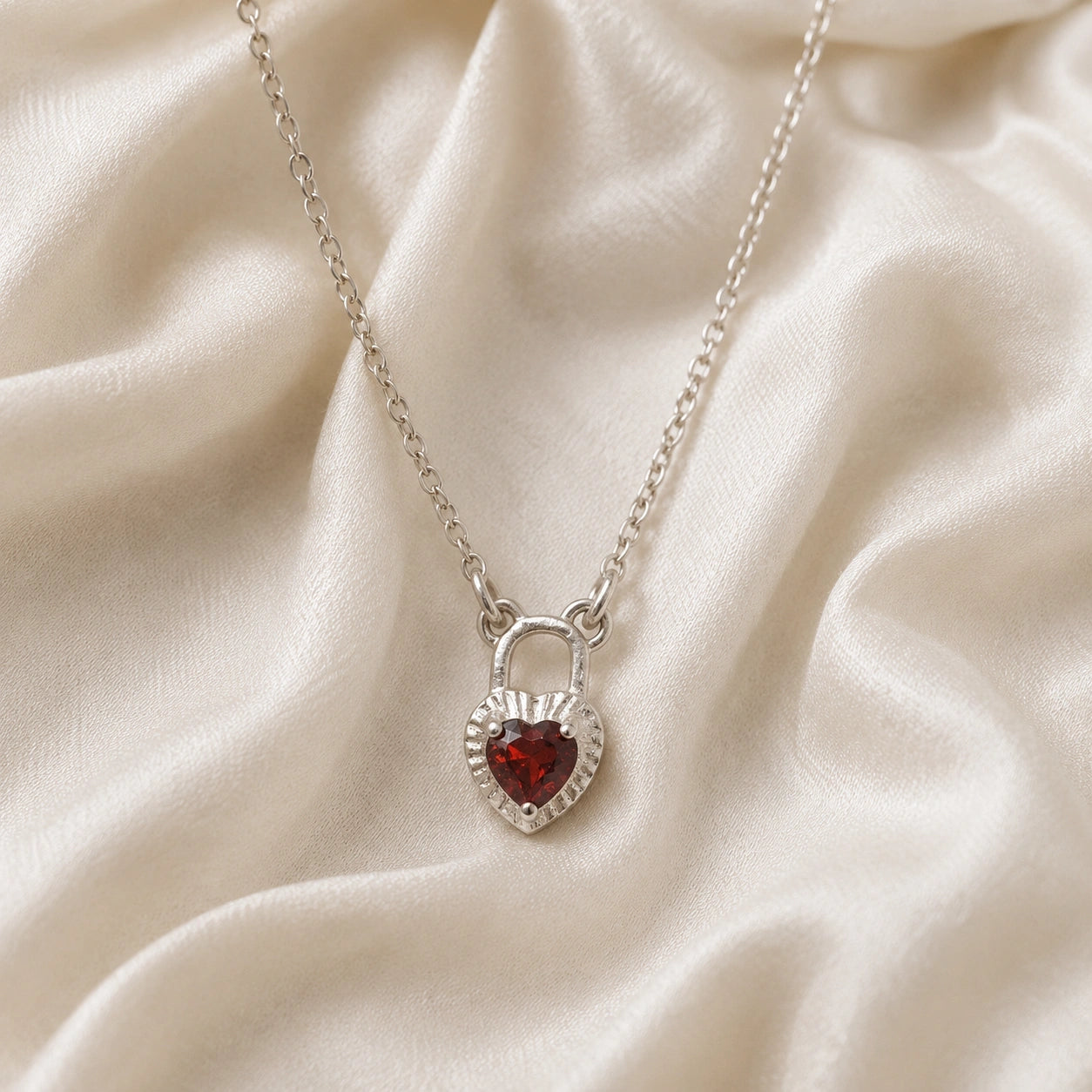 Heart_pendant_necklace_in_sterling_silver_front_angle_with_lock_design_and_garnet_stone_charm_on_soft_fabric_background