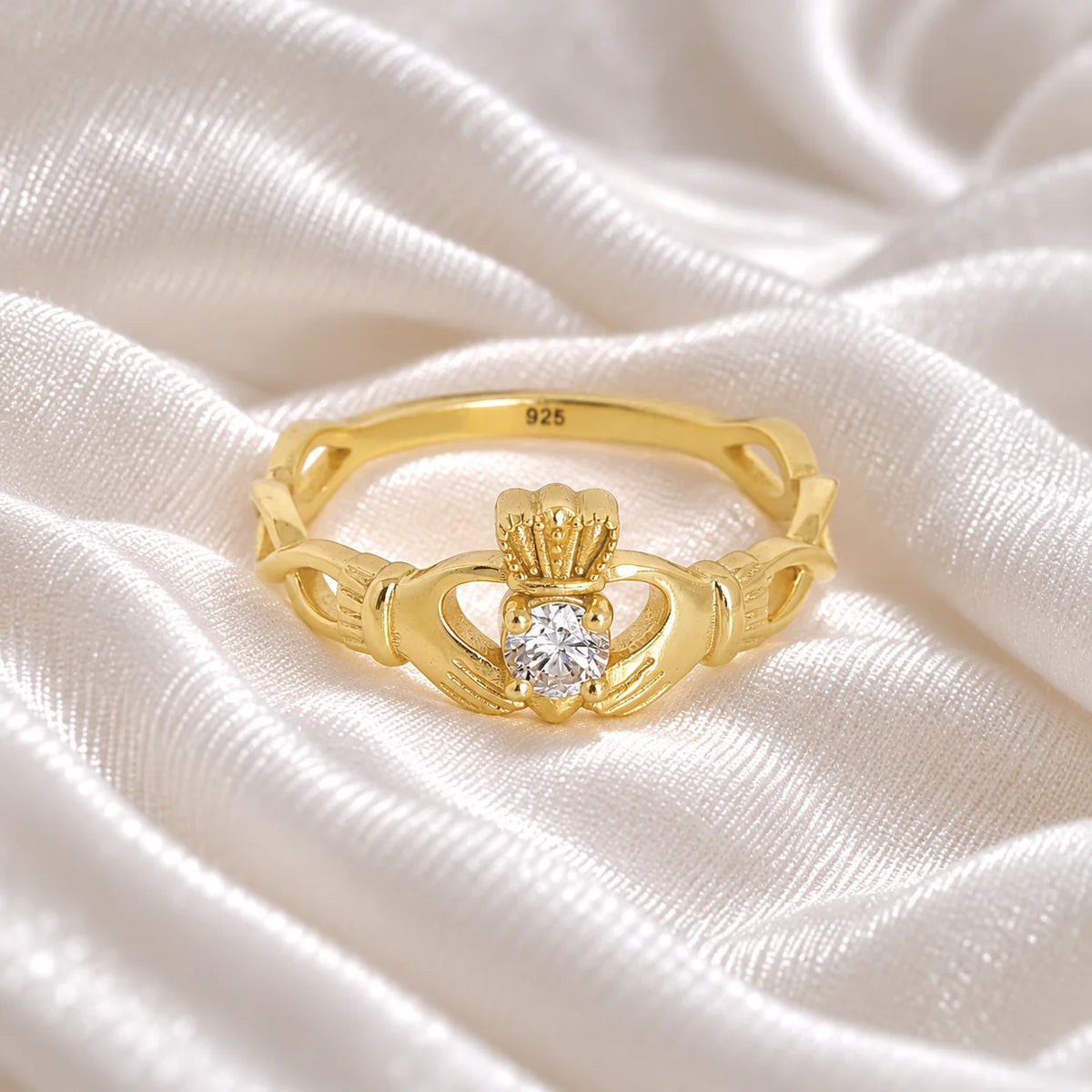 Heart_ring_in_gold_plated_silver_with_a_hand_a_heart_and_a_crown_design_at_front_angle_view_on_soft_fabric_background
