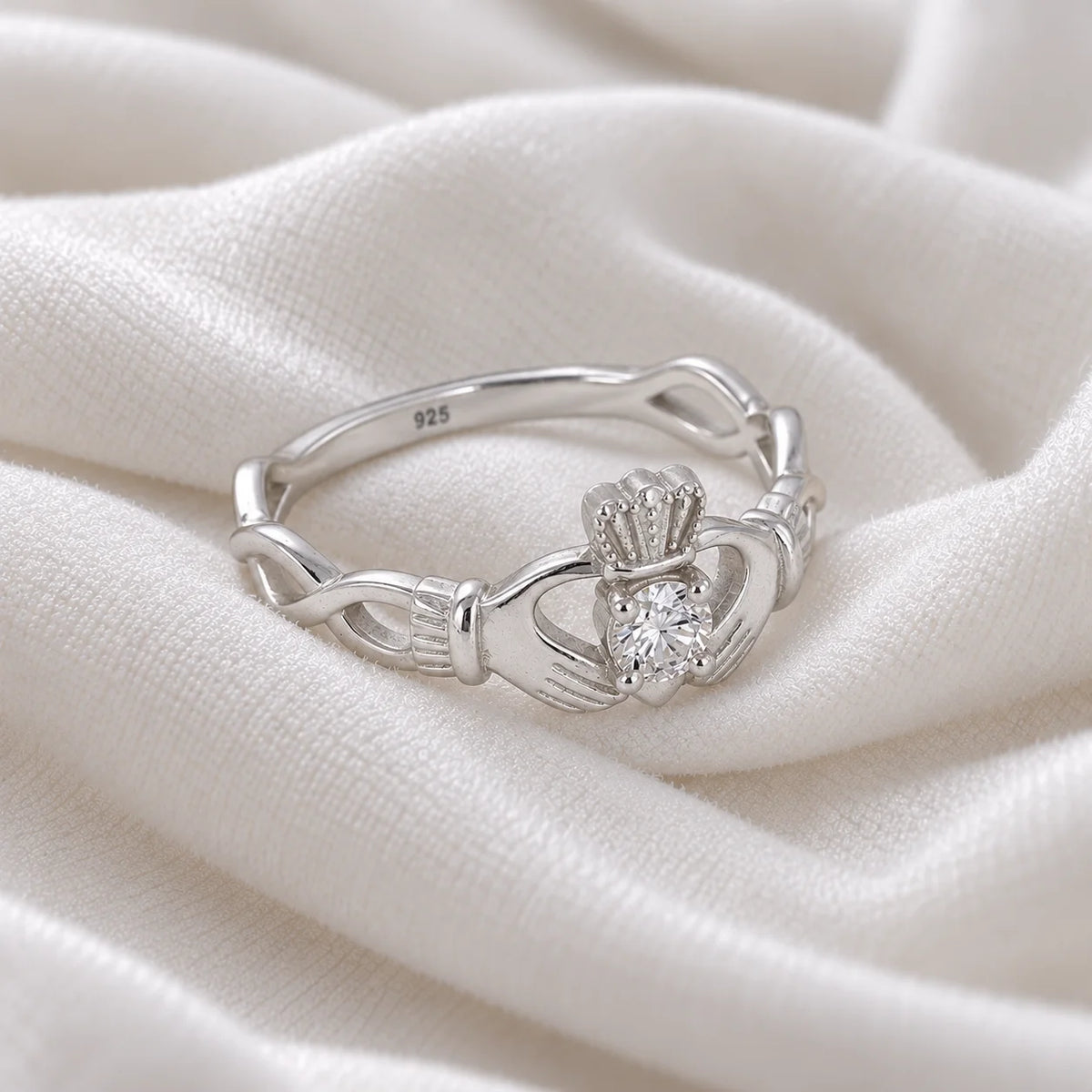 Heart_ring_in_sterling_silver_with_a_hand_a_heart_and_a_crown_design_at_side_angle_view_on_soft_fabric_background