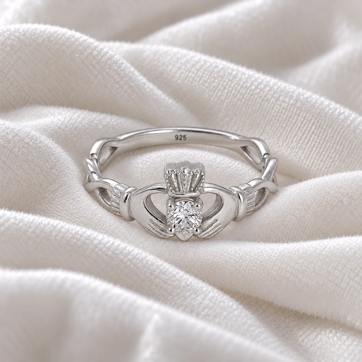 Heart_ring_in_sterling_silver_with_a_hand_a_heart_and_a_crown_design_at_front_angle_view_on_soft_fabric_background