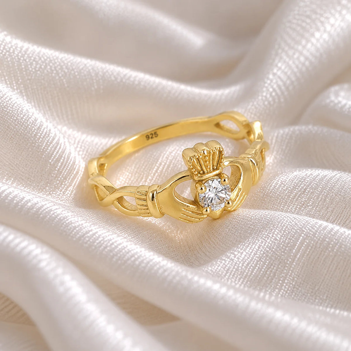 Heart_ring_in_gold_plated_silver_with_a_hand_a_heart_and_a_crown_design_at_side_angle_view_on_soft_fabric_background