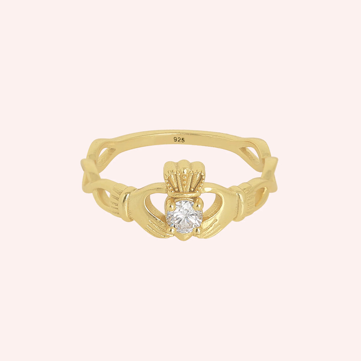 Heart_ring_in_gold_plated_silver_with_a_hand_a_heart_and_a_crown_design_at_front_angle_view_on_solid_pink_background