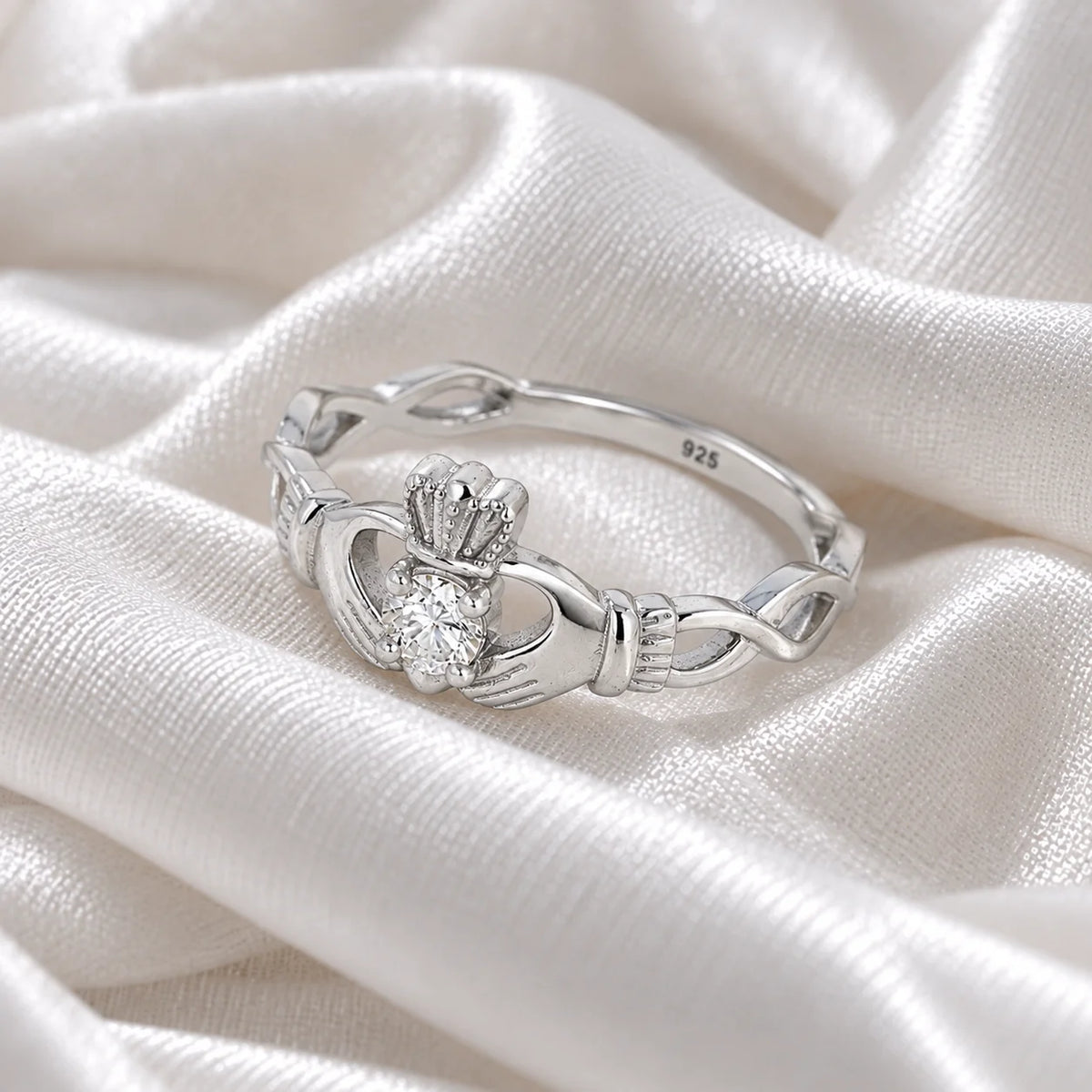 Heart_ring_in_sterling_silver_with_a_hand_a_heart_and_a_crown_design_at_side_angle_view_on_soft_fabric_background