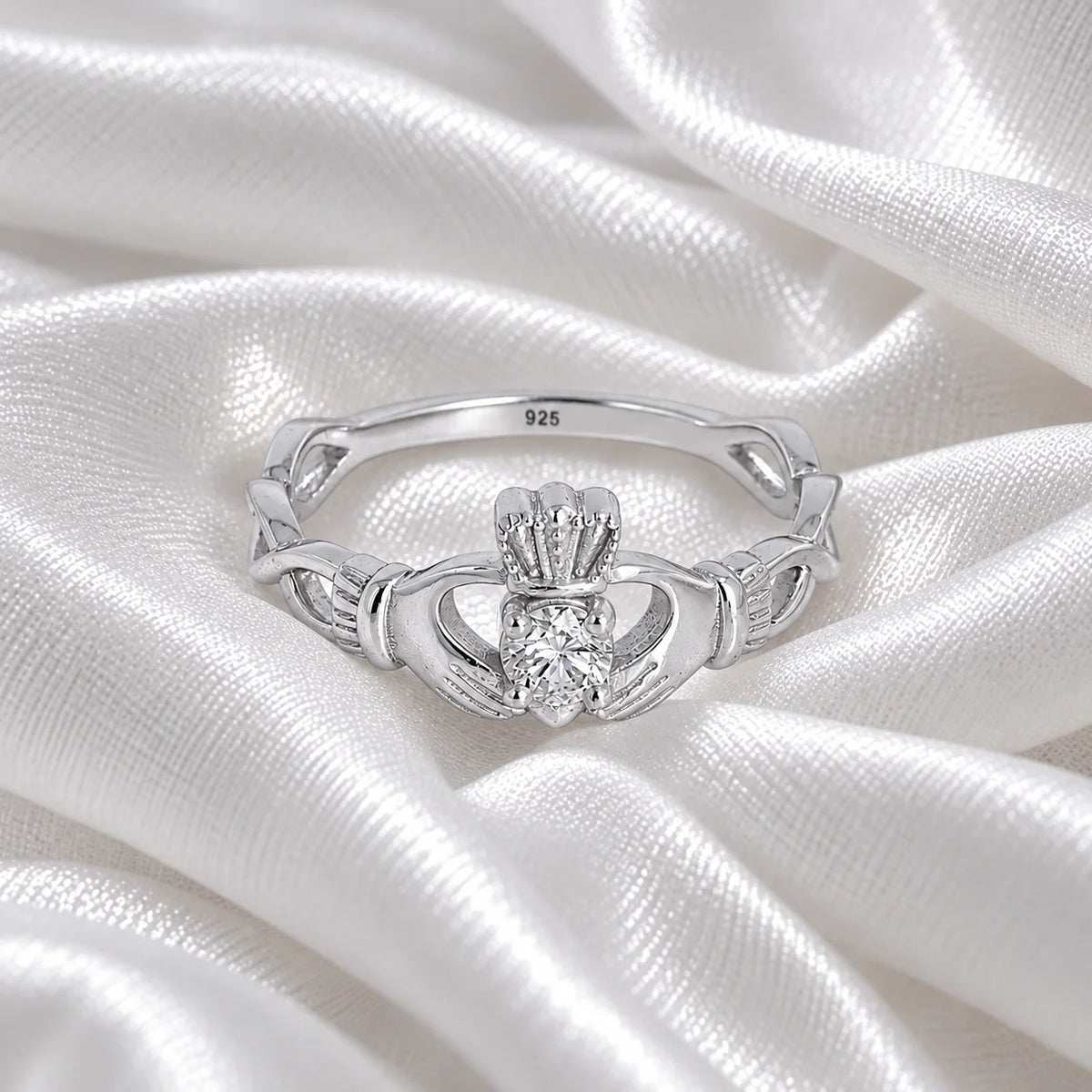 Heart_ring_in_sterling_silver_with_a_hand_a_heart_and_a_crown_design_at_front_angle_view_on_soft_fabric_background