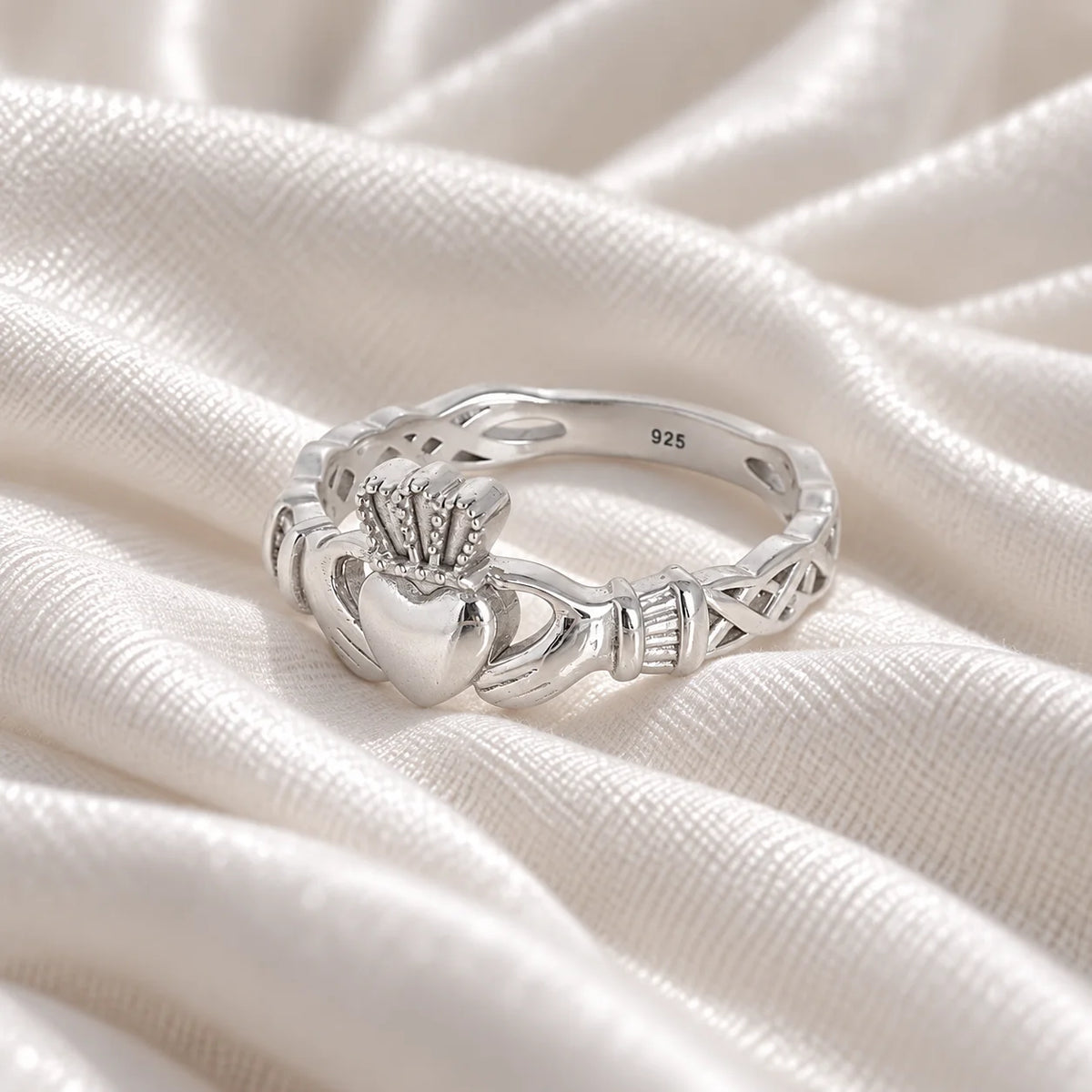 Heart_ring_in_sterling_silver_with_a_heart_hand_and_crown_design_at_slight_angle_view_on_soft_fabric_background