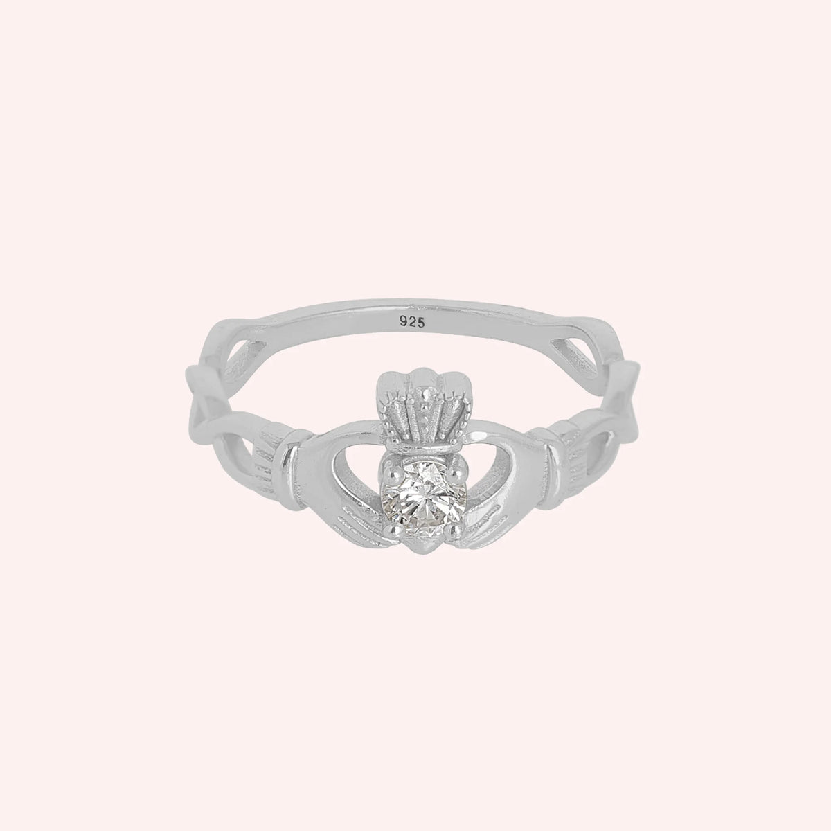 Heart_ring_in_sterling_silver_with_a_hand_a_heart_and_a_crown_design_at_front_angle_view_on_solid_pink_background