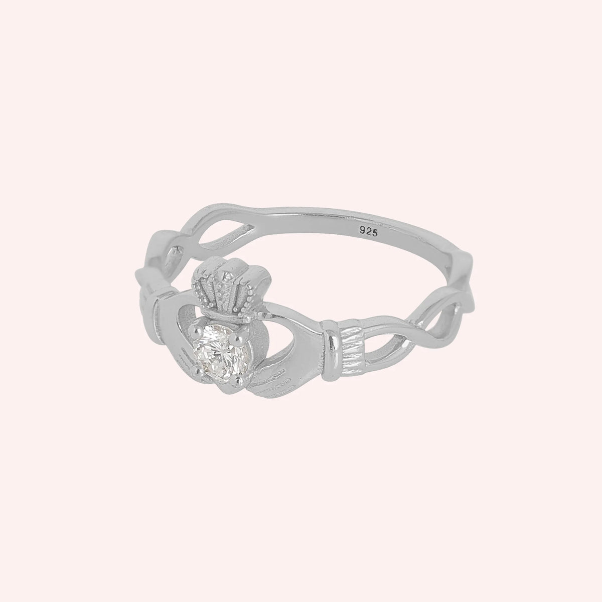 Heart_ring_in_sterling_silver_with_a_hand_a_heart_and_a_crown_design_at_side_angle_view_on_solid_pink_background