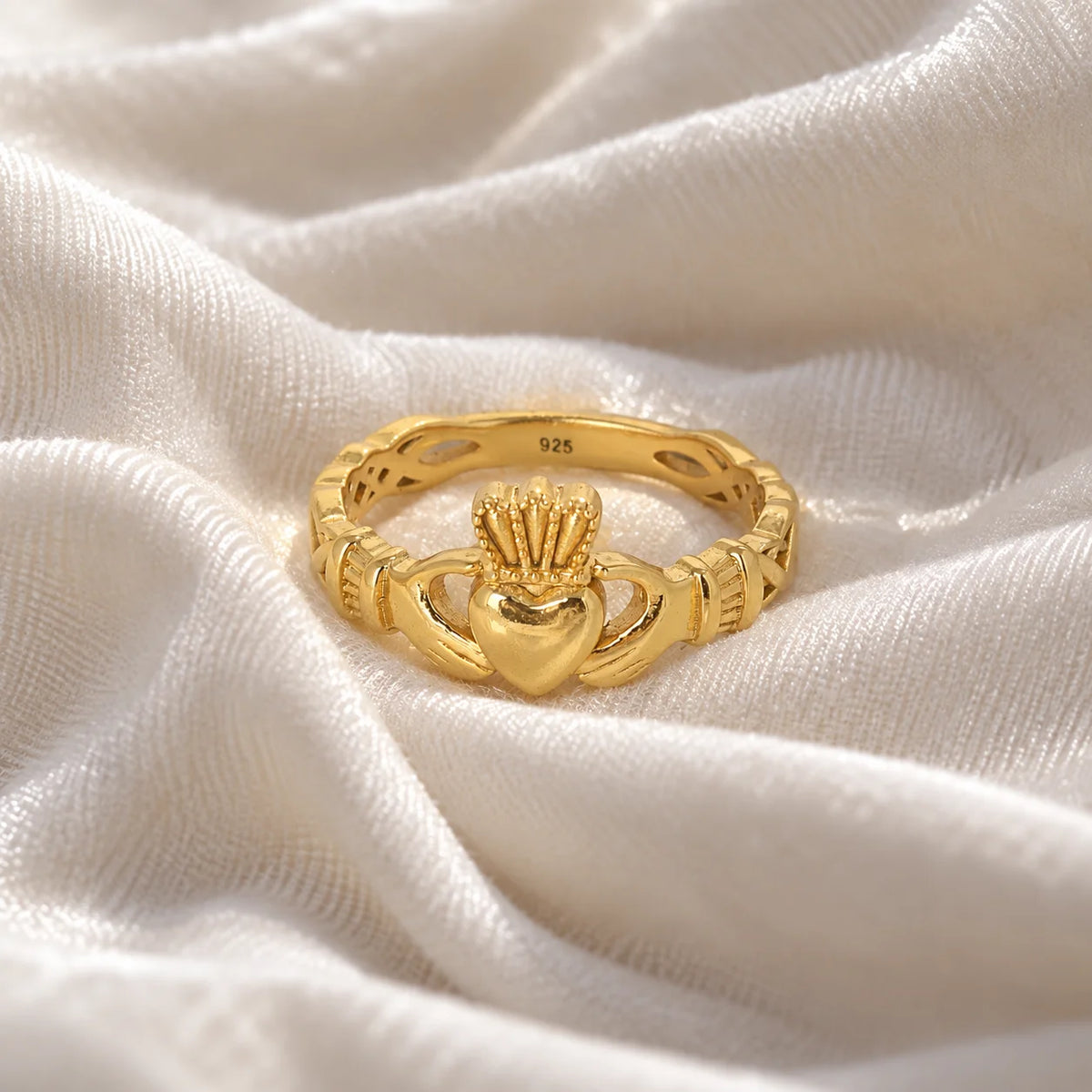 Heart_ring_in_gold_plated_silver_with_a_heart_hand_and_crown_design_at_front_angle_view_on_soft_fabric_background