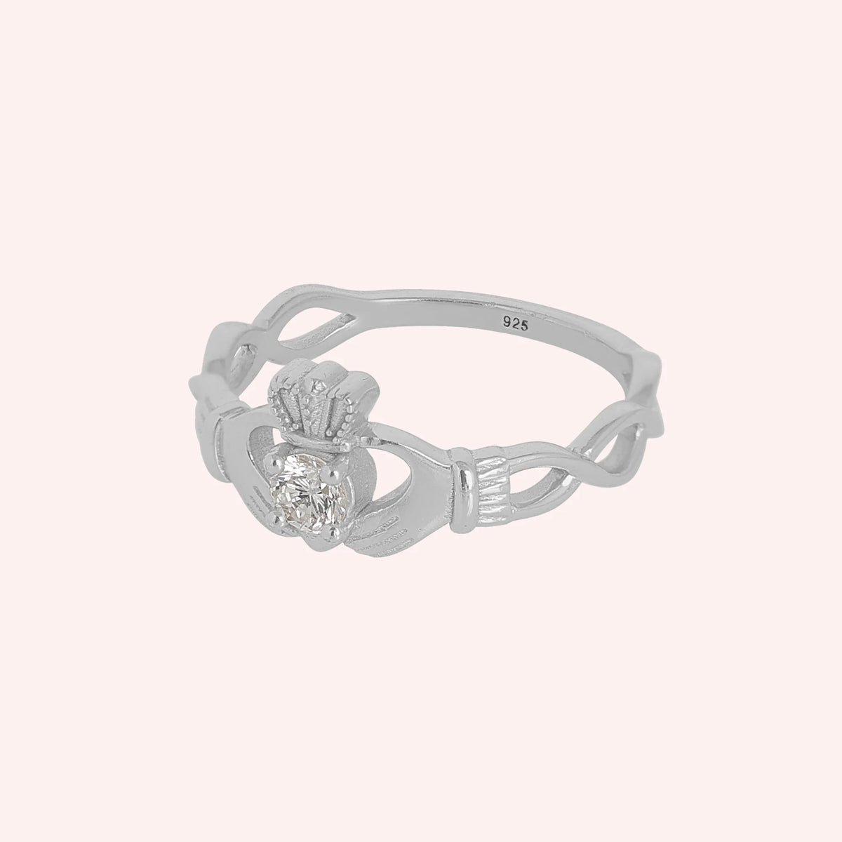 Heart_ring_in_sterling_silver_with_a_hand_a_heart_and_a_crown_design_at_side_angle_view_on_solid_pink_background