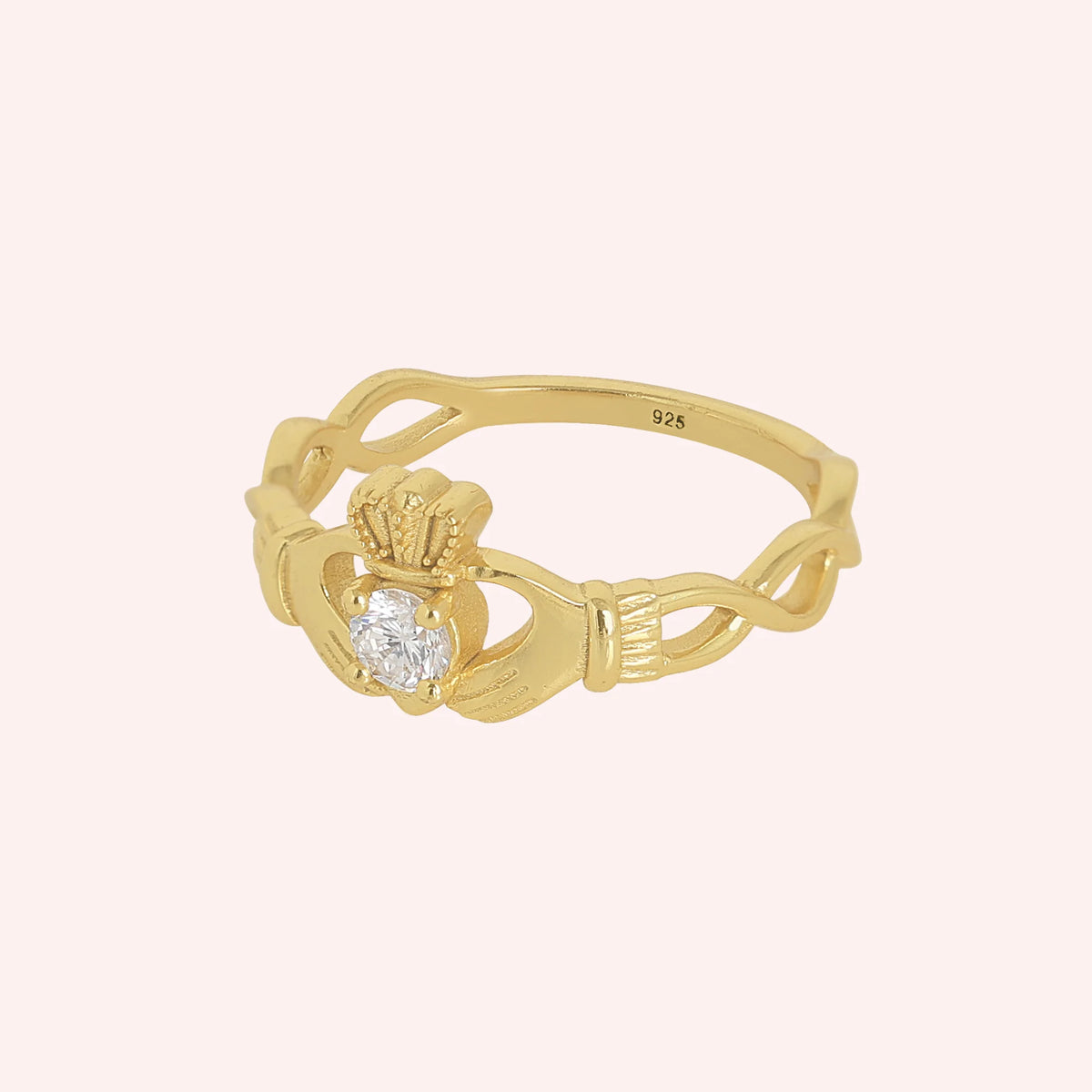 Heart_ring_in_gold_plated_silver_with_a_hand_a_heart_and_a_crown_design_at_side_angle_view_on_solid_pink_background