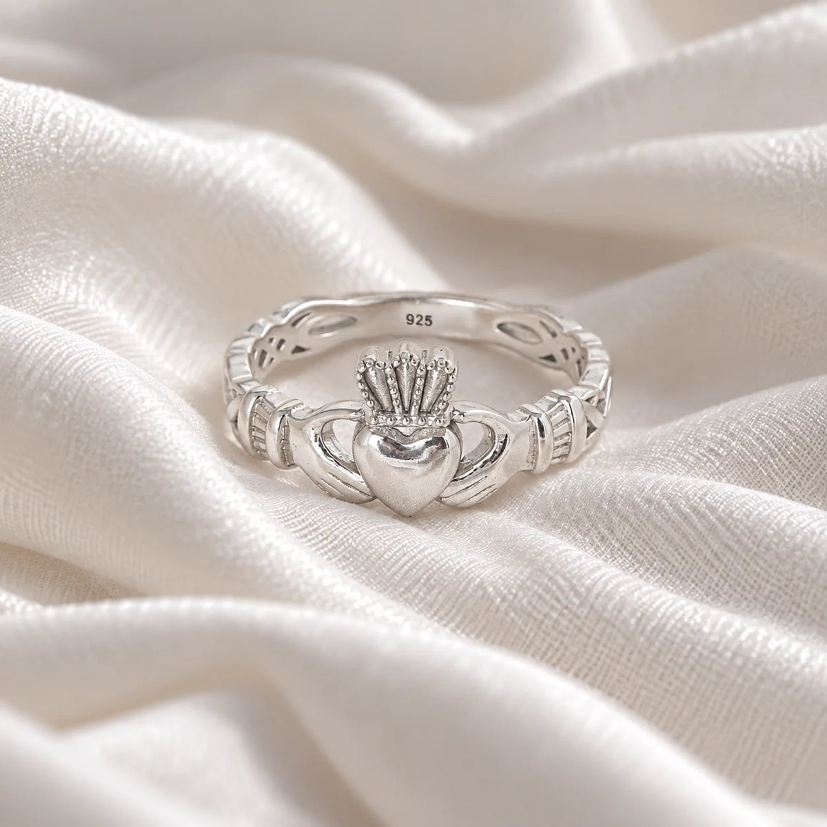Heart_ring_in_sterling_silver_with_a_heart_hand_and_crown_design_at_front_angle_view_on_soft_fabric_background