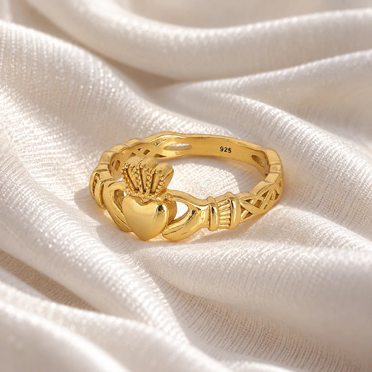 Heart_ring_in_gold_plated_silver_with_a_heart_hand_and_crown_design_at_slight_angle_view_on_soft_fabric_background