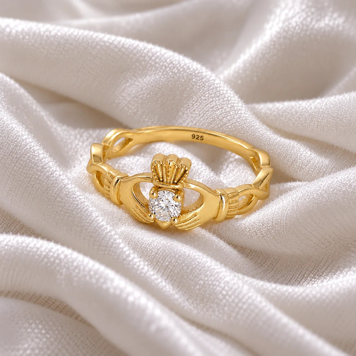 Heart_ring_in_gold_plated_silver_with_a_hand_a_heart_and_a_crown_design_at_side_angle_view_on_soft_fabric_background