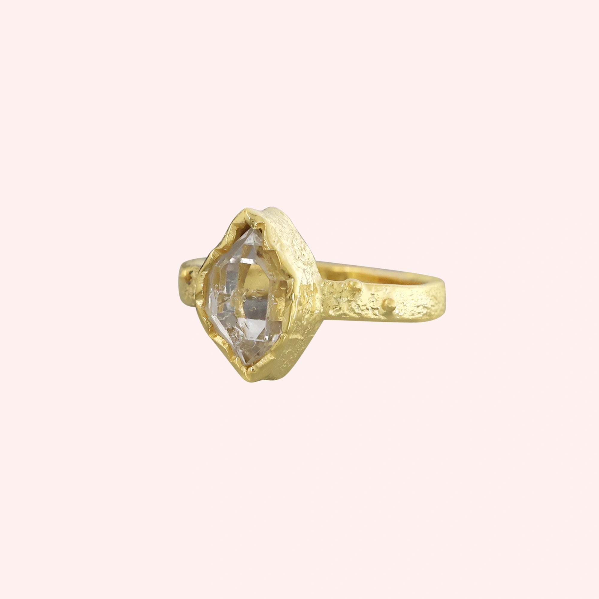Herkimer_diamond_ring_gold_plated_silver_band_with_raw_herkimer_stone_shown_in_slightly_angled_view_on_solid_pink_background