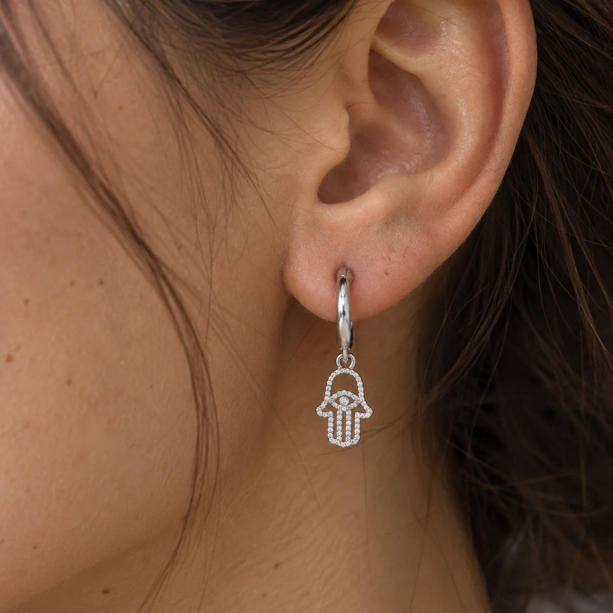 Hoop_earrings_in_sterling_silver_with_a_hamsa_hand_design_worn_by_a_model