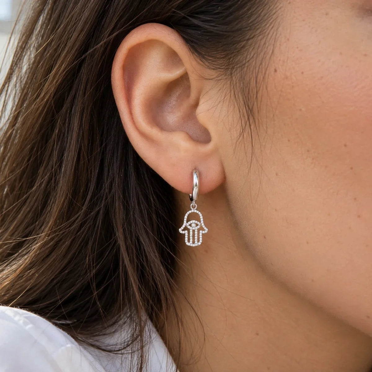 Hoop_earrings_in_sterling_silver_with_hamsa_hand_design_and_CZ_stones_at_front_angle_view_worn_by_a_model