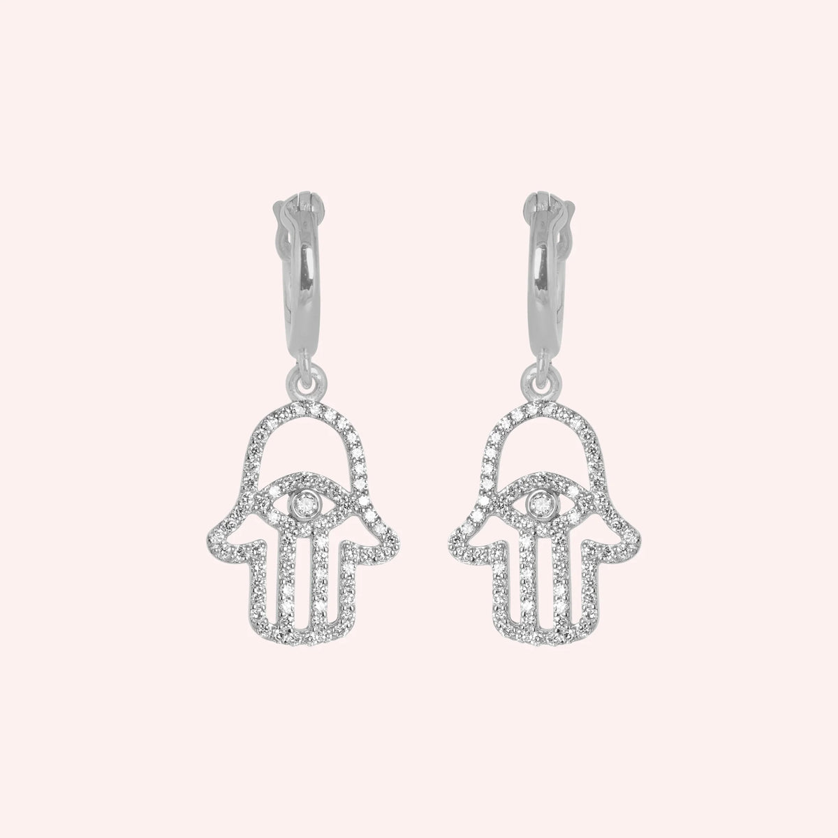 Hoop_earrings_in_sterling_silver_with_hamsa_hand_design_and_CZ_stones_at_front_angle_view_on_solid_pink_background