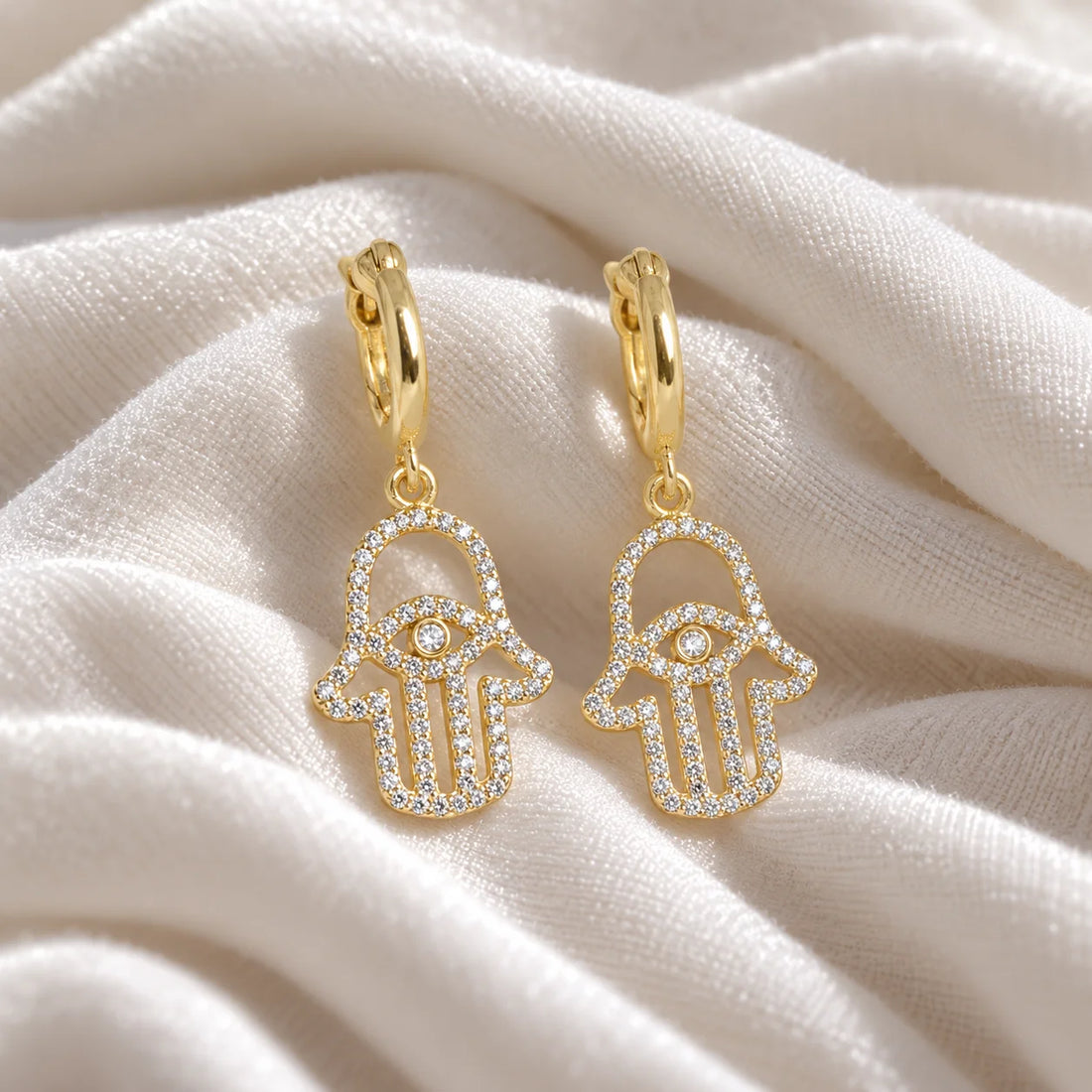 Hoop_earrings_in_gold_plated_silver_with_a_hamsa_hand_design_at_front_angle_view_on_soft_fabric_background