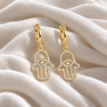 Hoop_earrings_in_gold_plated_silver_with_a_hamsa_hand_design_at_front_angle_view_on_soft_fabric_background