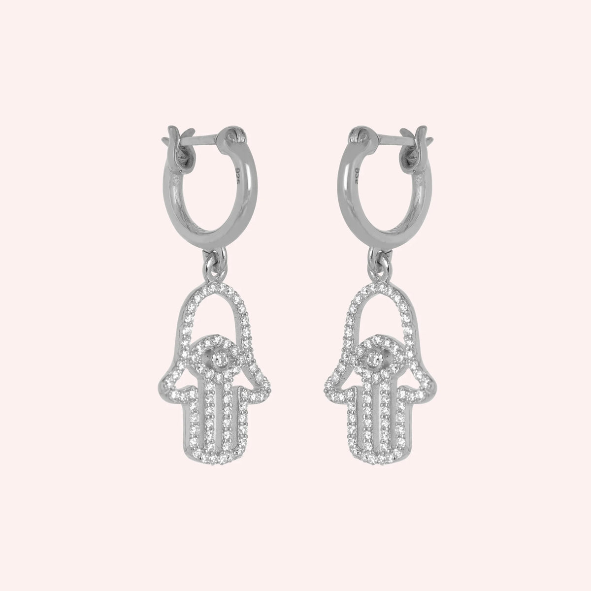 Hoop_earrings_in_sterling_silver_with_hamsa_hand_design_and_CZ_stones_at_side_angle_view_on_solid_pink_background